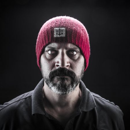 A man with a severe expression, wearing a pink beanie and a black shirt, symbolising Behavioural Safety.