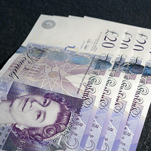 Anti Money Laundering training can help you identify fake money like British 20-pound notes fanned out on a dark surface. It features a portrait of Queen Elizabeth II and blue and purple colour schemes.